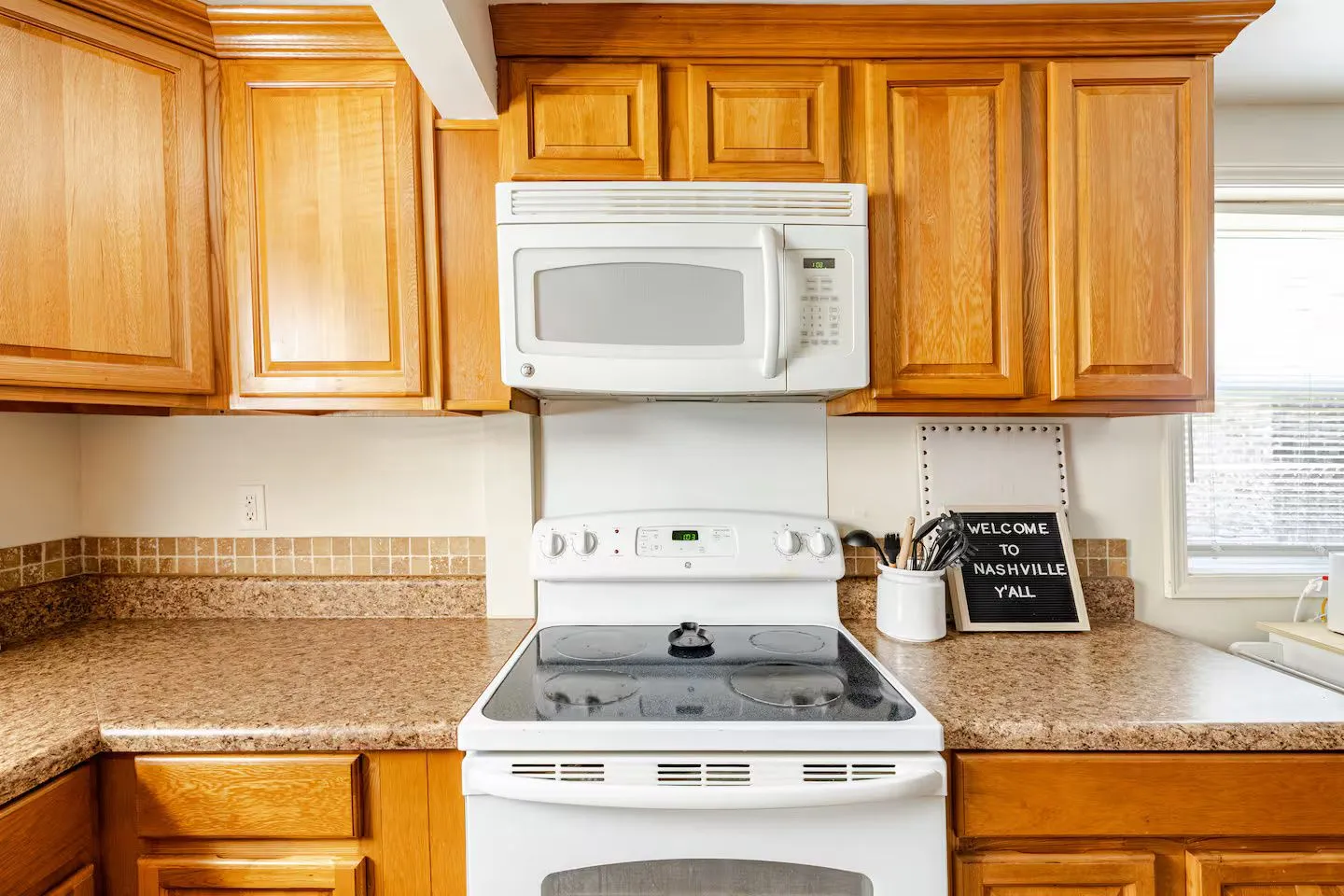 Kitchen counter and electric range flanked by wood cabinets with an over-the-range microwave.