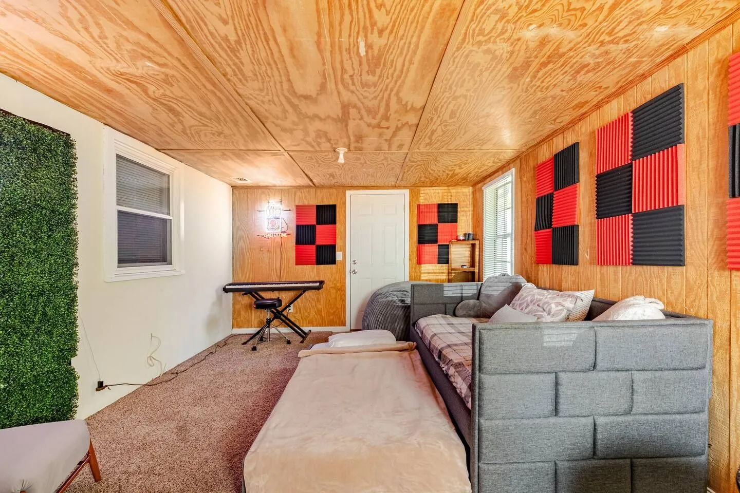A bonus room with wood-paneled walls and ceiling, carpeted flooring, a daybed with a trundle, a keyboard, and acoustic foam panels.