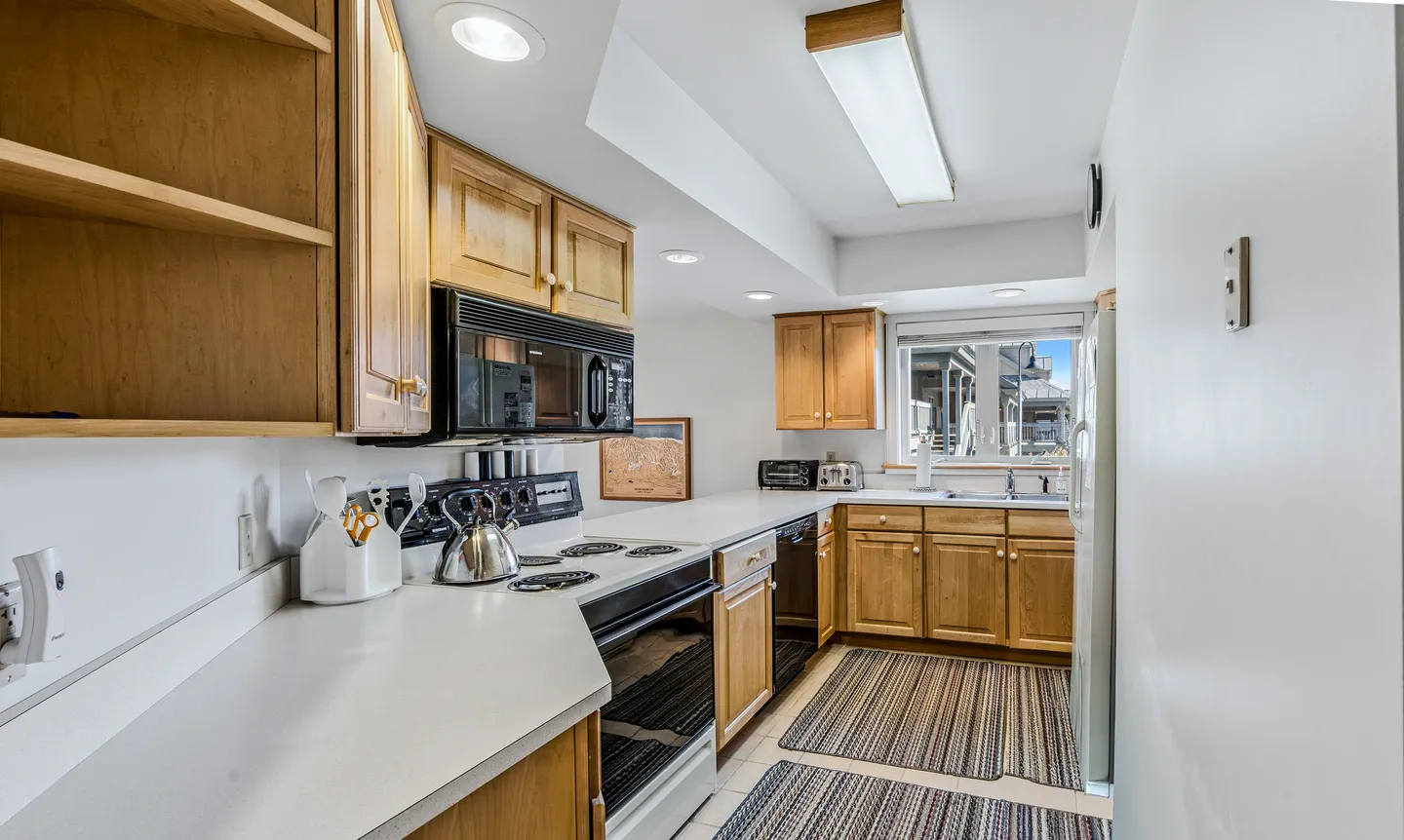 Kitchen with wooden cabinetry, white countertops, black microwave and stove, and a window above the sink.