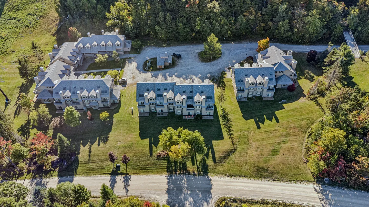 Aerial view of a multi-building residential complex surrounded by green lawns and dense trees.