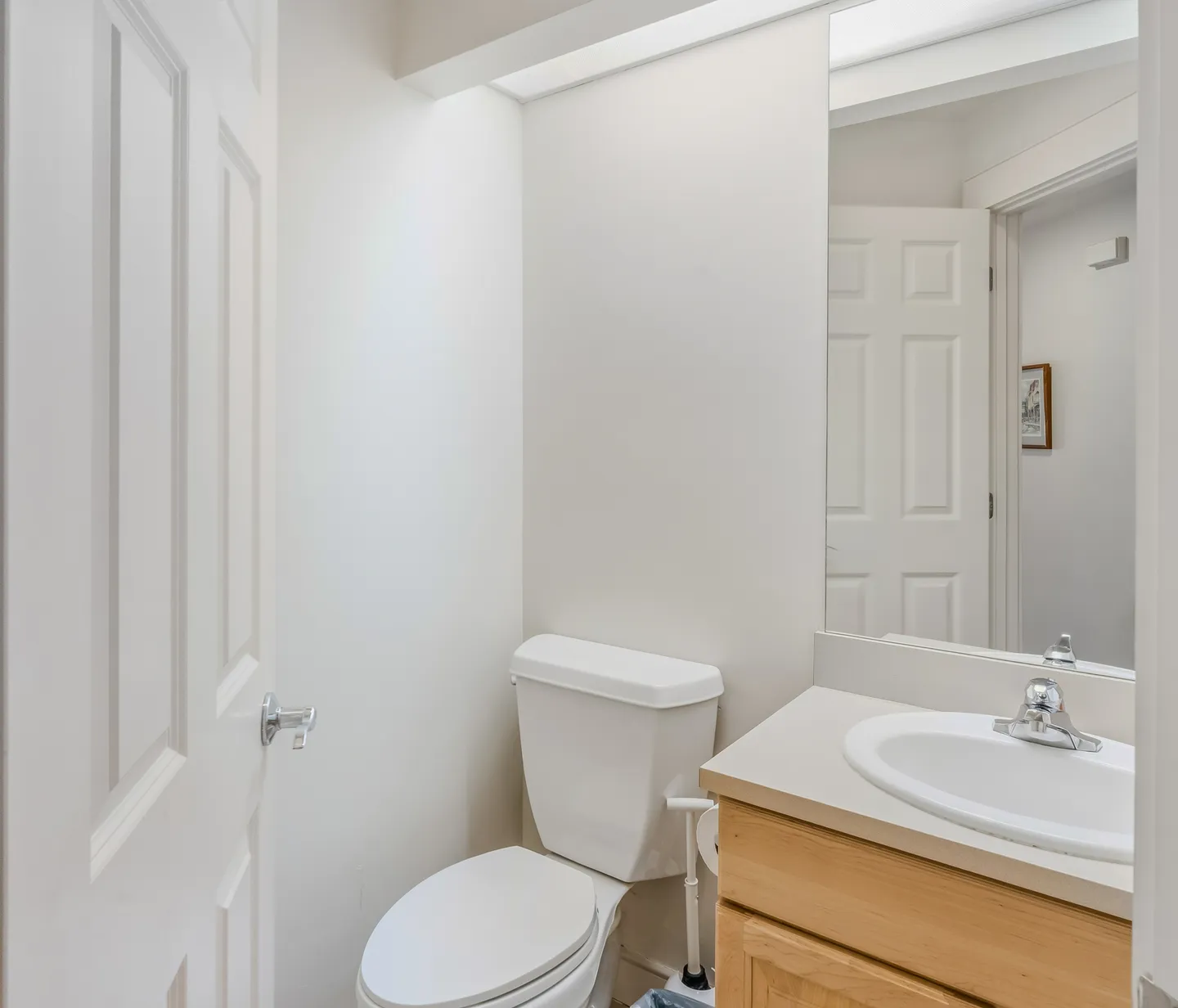 Bathroom with a white toilet, light wood vanity with white sink, and mirror reflecting a doorway.