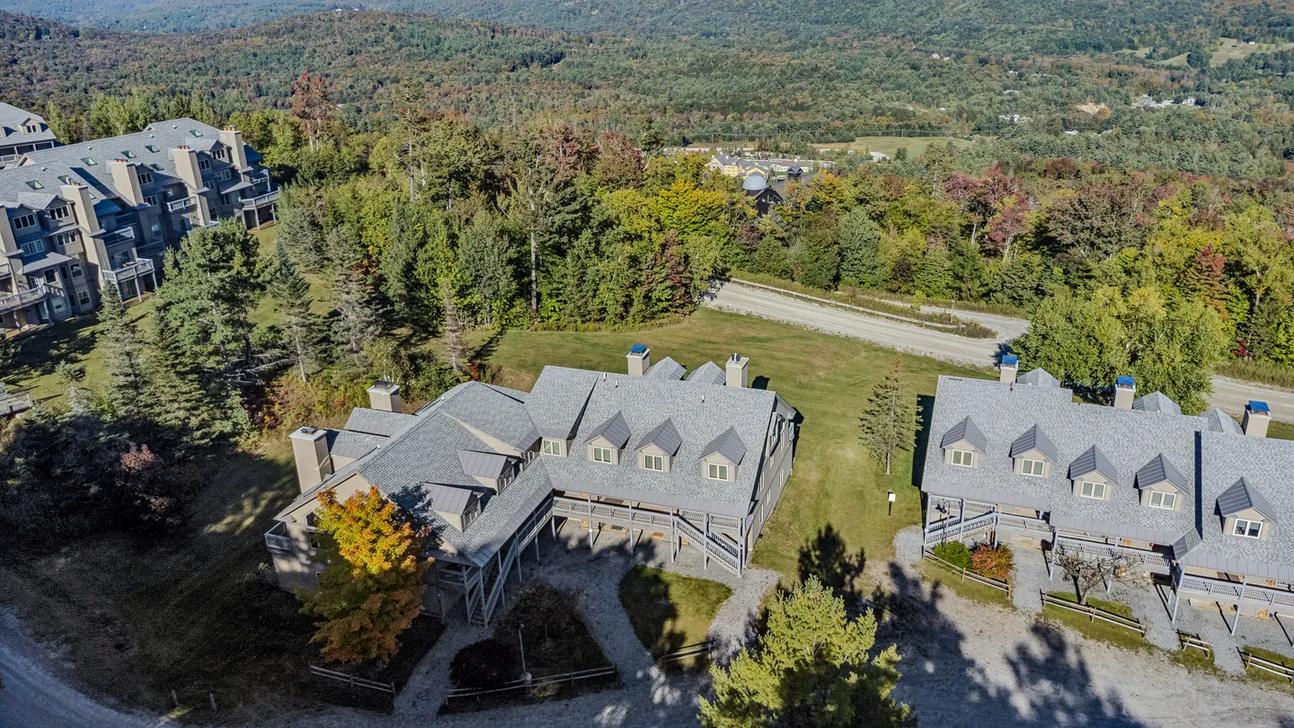 Aerial view of multi-story mountain lodges surrounded by autumn trees and rolling forested hills.