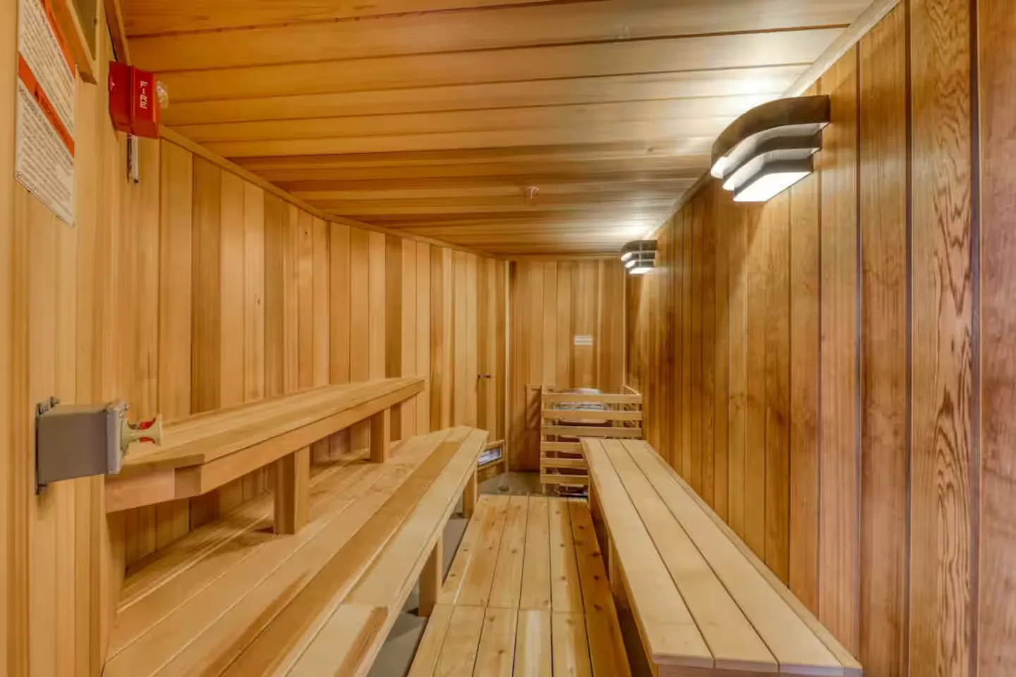 Interior view of a wood-paneled sauna with multi-tiered wooden benches and wall-mounted lighting.