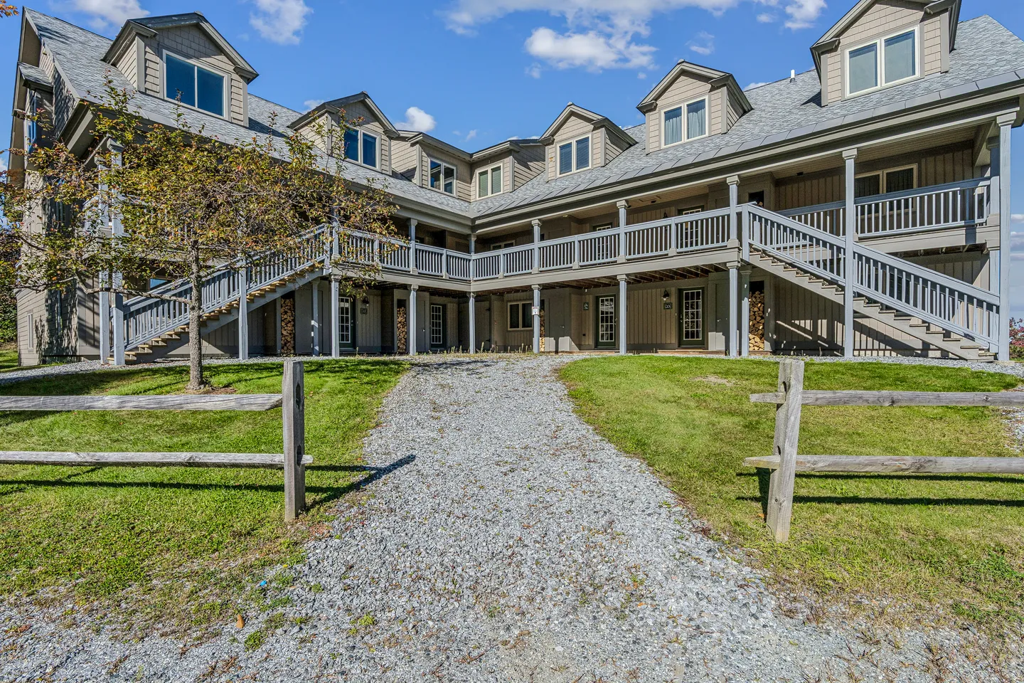 Exterior view of a multi-story building with gray siding, dormer windows, outdoor staircases, and a gravel pathway in front.