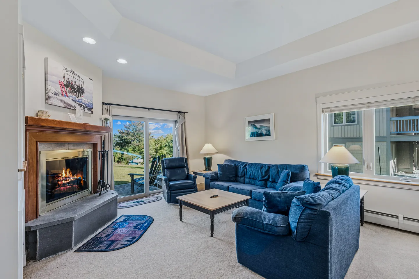 Living room with blue sofas, a coffee table, a lit fireplace, and sliding glass doors opening to an outdoor patio.