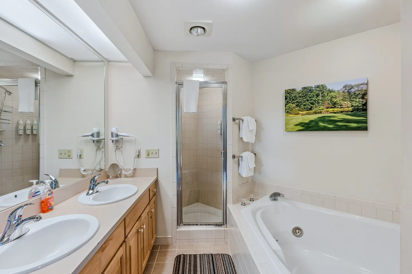 Bathroom featuring a double-sink vanity, a tiled soaking tub, and a glass-door walk-in shower.