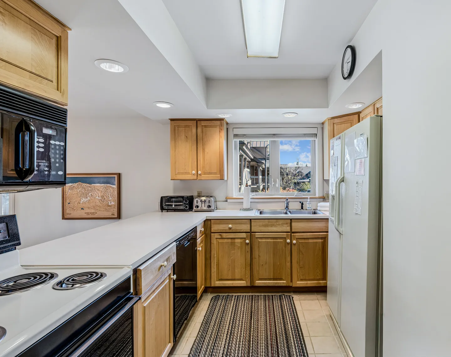 Kitchen with wooden cabinetry, white countertops, a double sink under a window, and electric appliances.