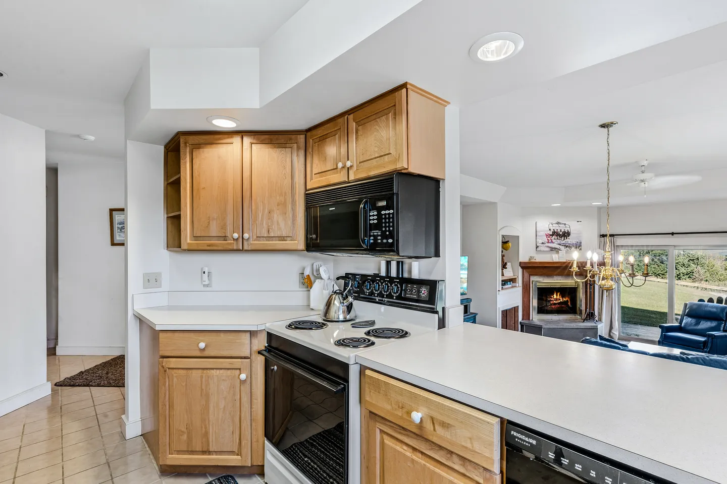 Kitchen counter and electric range looking past upper cabinets toward a living room with a fireplace.