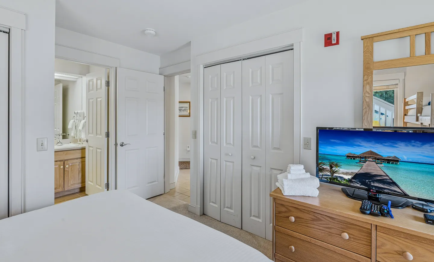 Bedroom with view toward ensuite bathroom, closet bifold doors, and television on a wooden dresser.