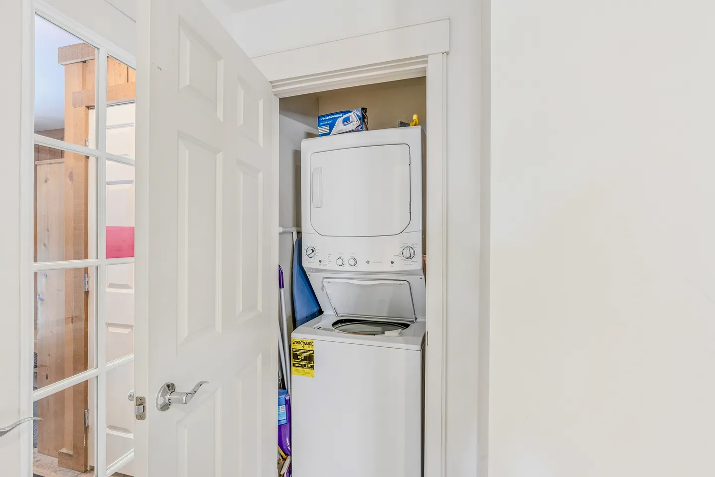 A stacked white washer and dryer unit inside a small closet with an open white door.