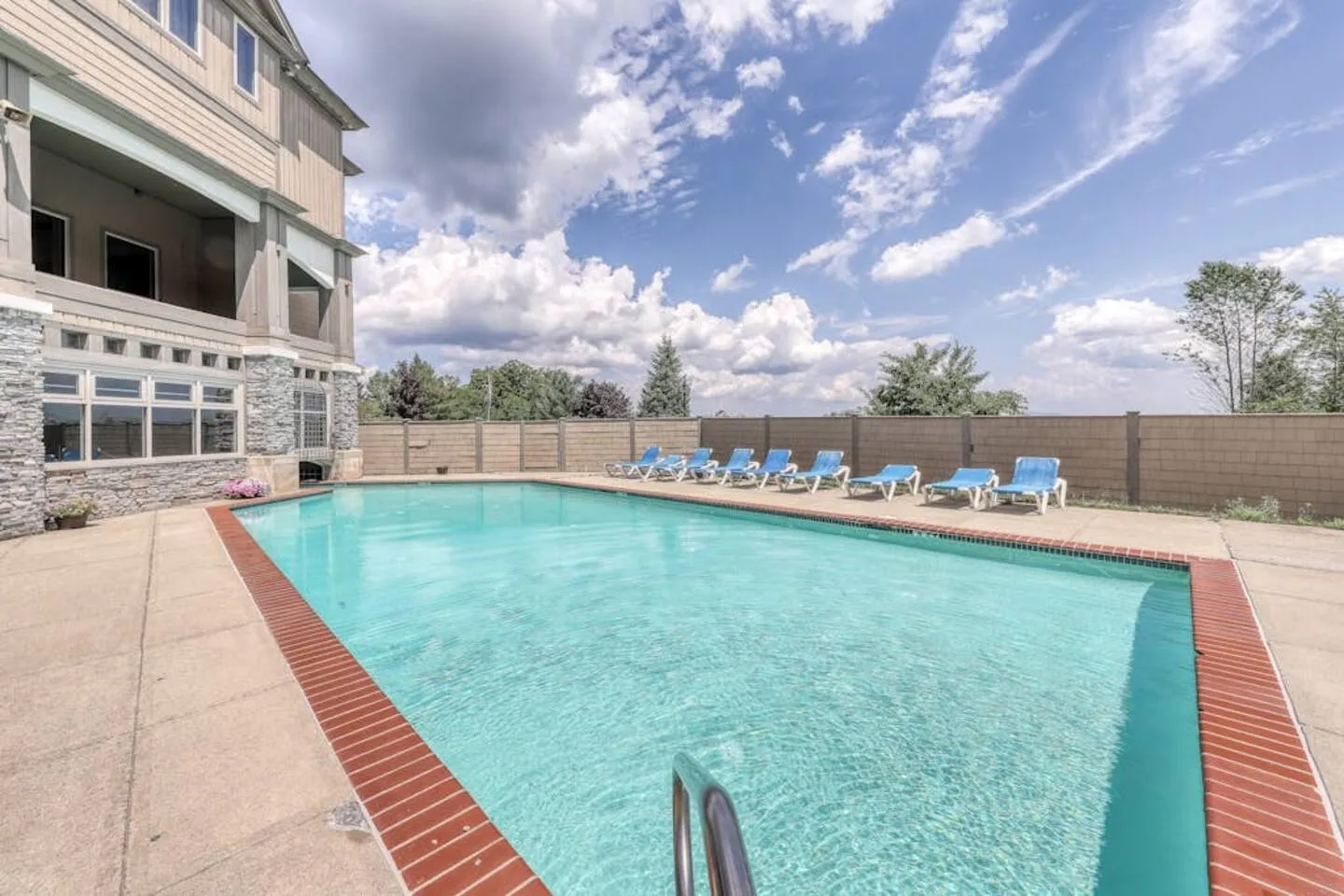 Outdoor swimming pool bordered by red brick coping, a concrete deck, and several lounge chairs along a perimeter wall.