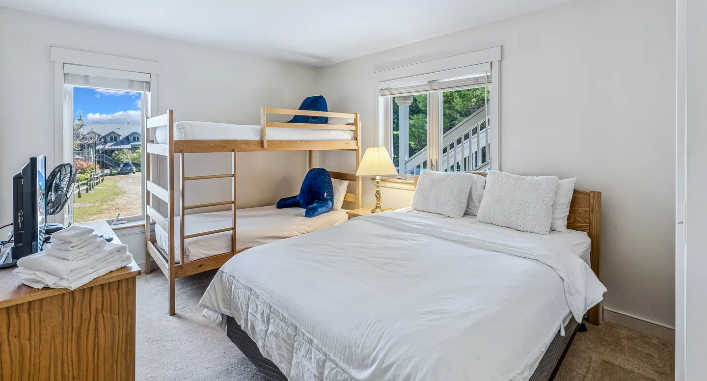 Bedroom with a queen-sized bed, wooden bunk beds, and two windows showing outdoor scenery.