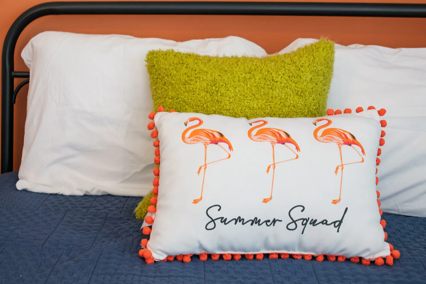 Close-up of decorative pillows on a bed, including a white pillow with pink flamingos that reads Summer Squad.