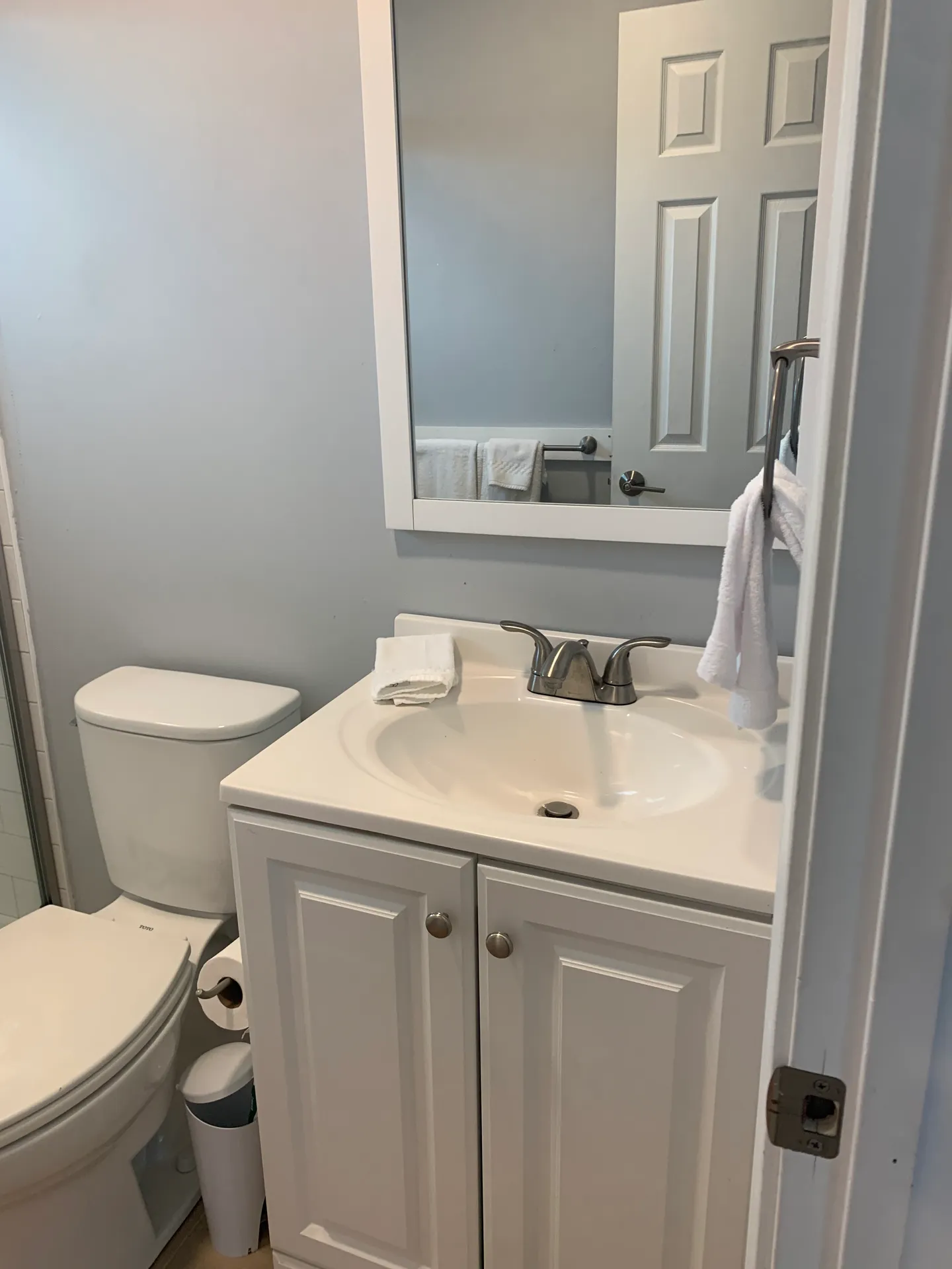 Bathroom showing a white vanity with a sink, framed mirror, toilet, and towel ring.