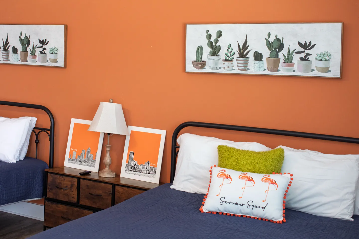 Bedroom with bold orange walls, black metal bed frames with blue bedspreads, and succulent wall art above each bed.