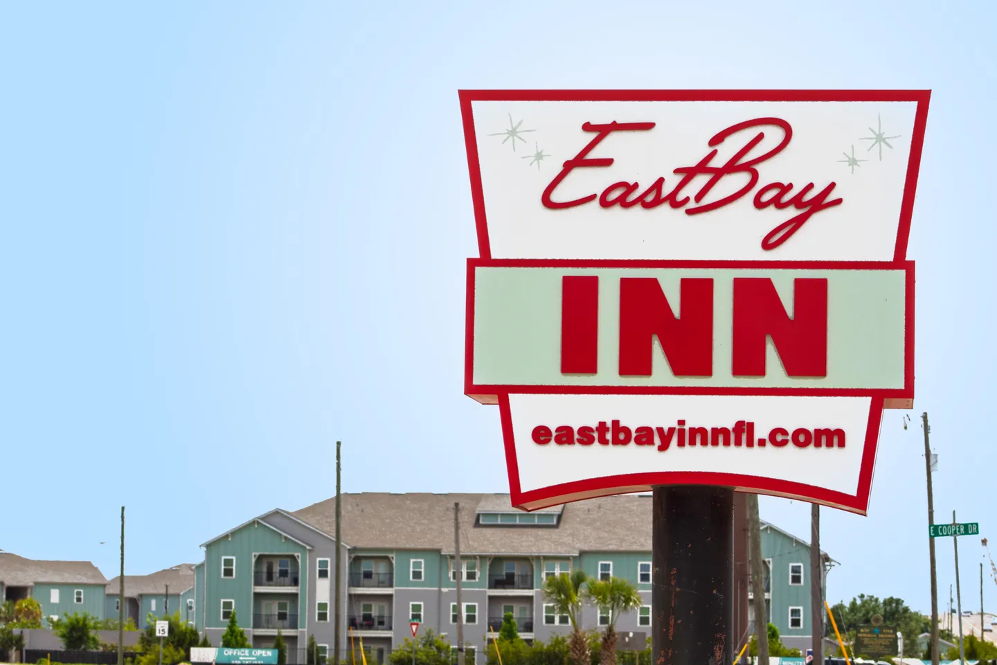 A retro-style outdoor sign for East Bay Inn with a multistory building in the background against a clear blue sky.