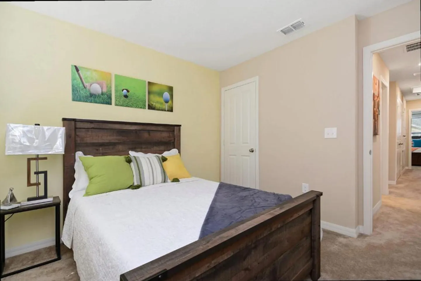Bedroom with a wooden bed frame, green and yellow accent pillows, golf-themed wall art, and an open doorway leading to a hallway.