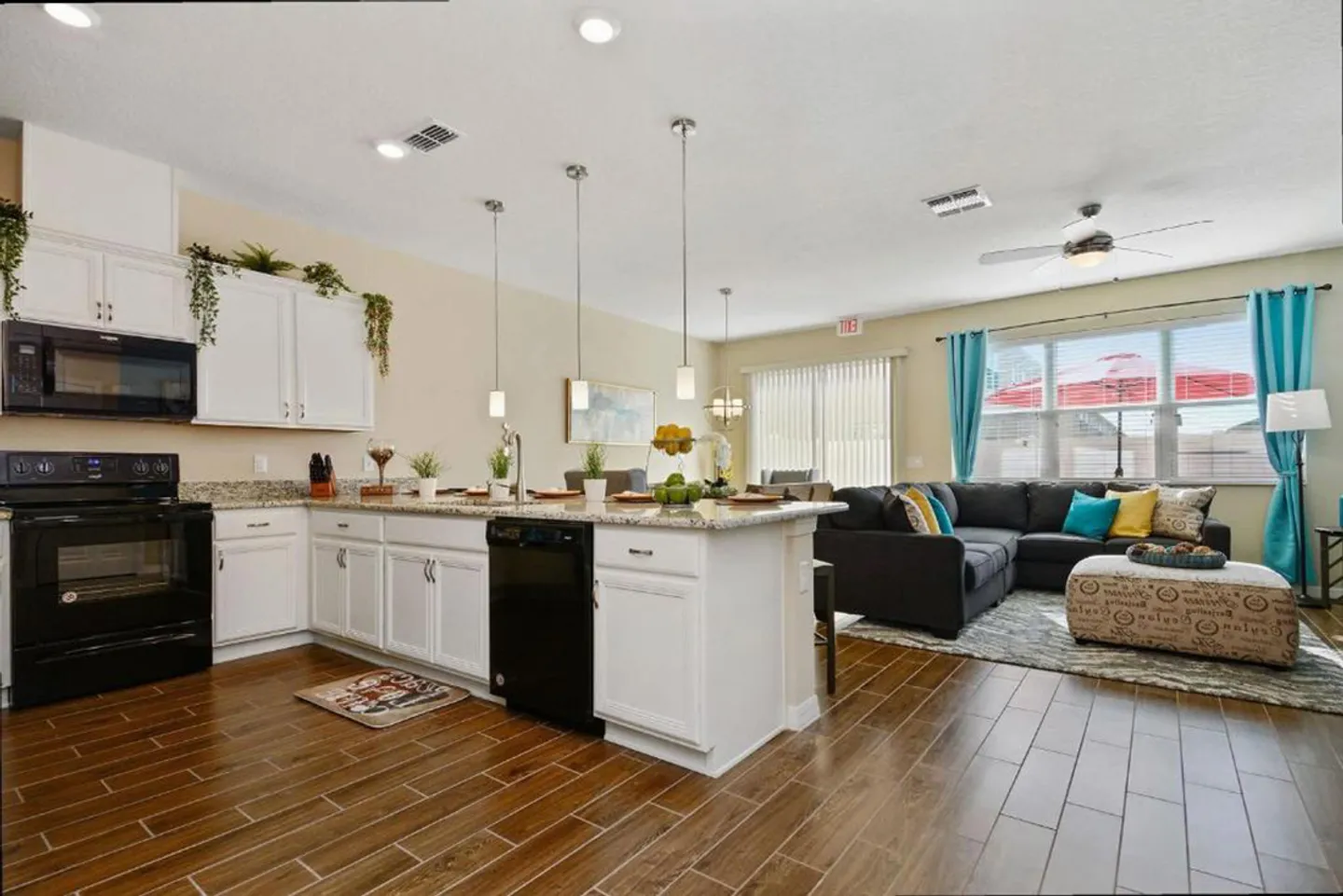 Open-concept kitchen and living room with wood-look tile flooring, white cabinets, island counter, and a sectional couch.