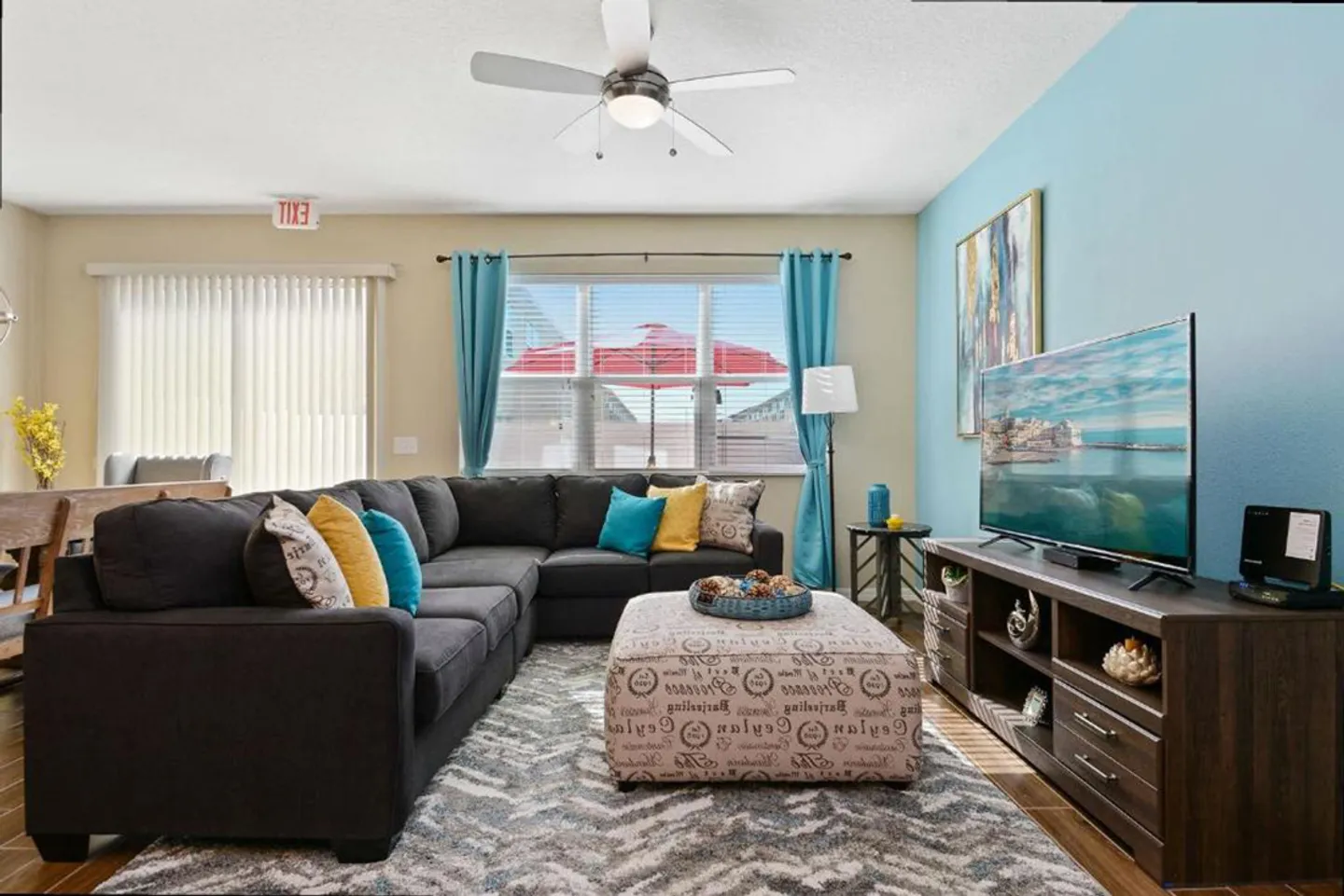 Living room with a large dark sectional sofa, printed ottoman, patterned area rug, and flat-screen TV on a media console.
