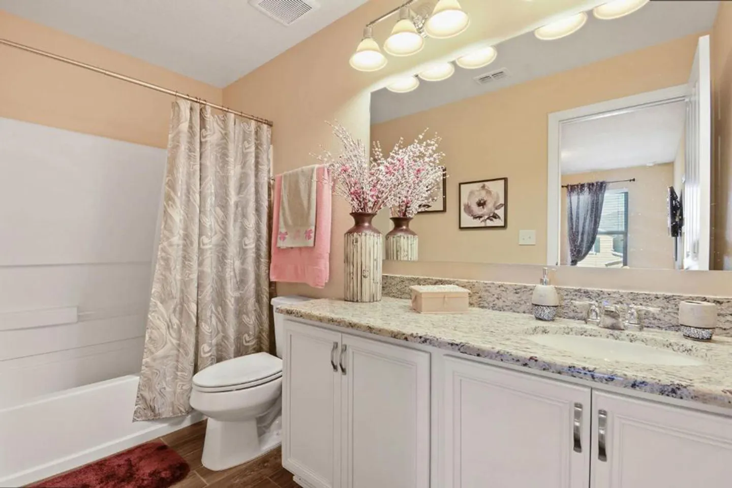 Bathroom with a white vanity, speckled countertop, large mirror, toilet, and shower-tub combination.