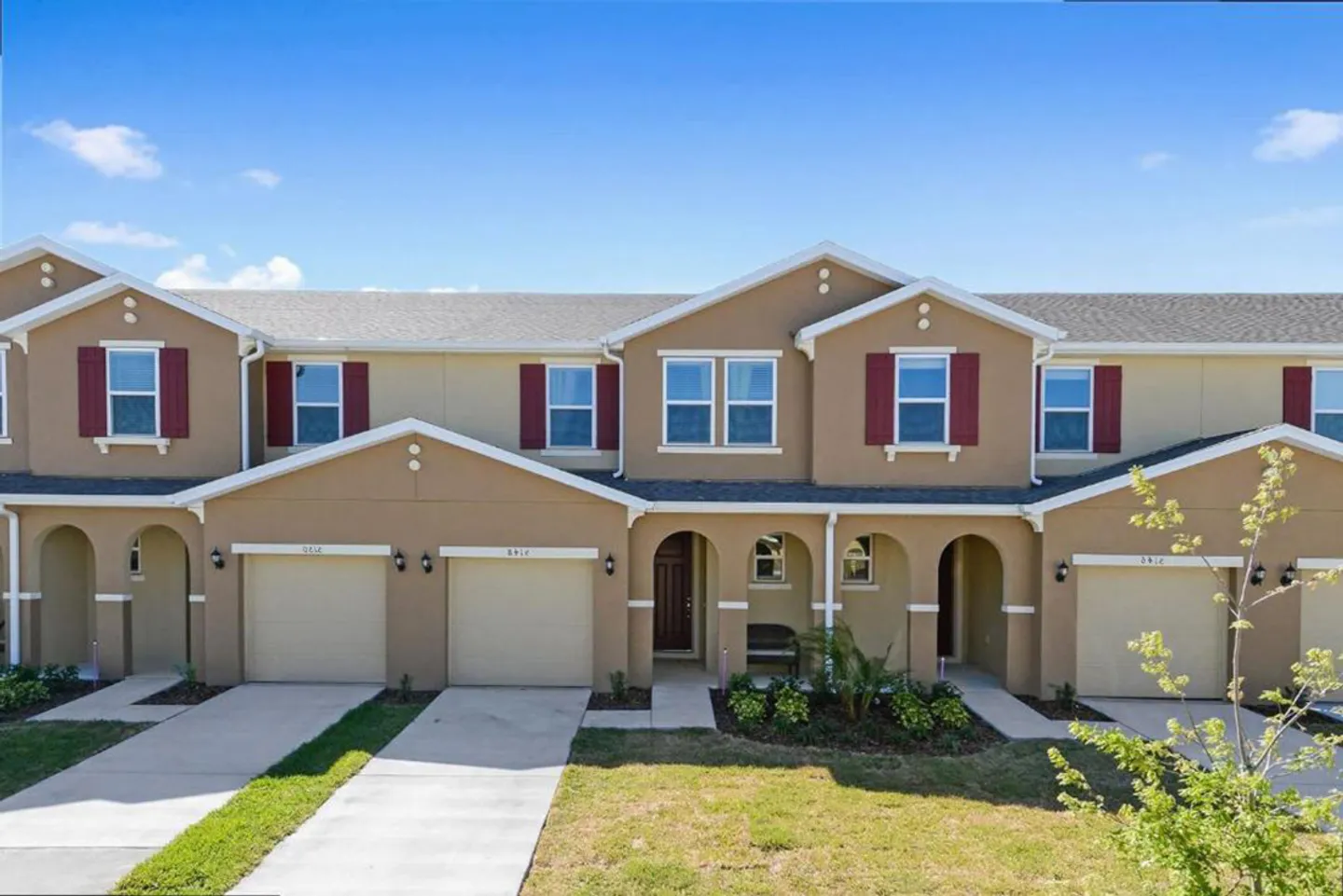 Exterior front facade of a two-story beige townhome with red decorative shutters, arched entryways, and attached garages.