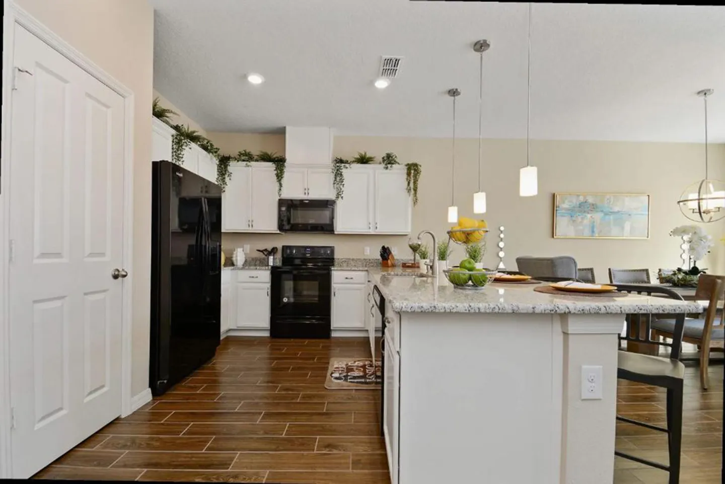 Kitchen with white cabinetry, black appliances, a granite-topped island with pendant lights, and wood-look tile floors.