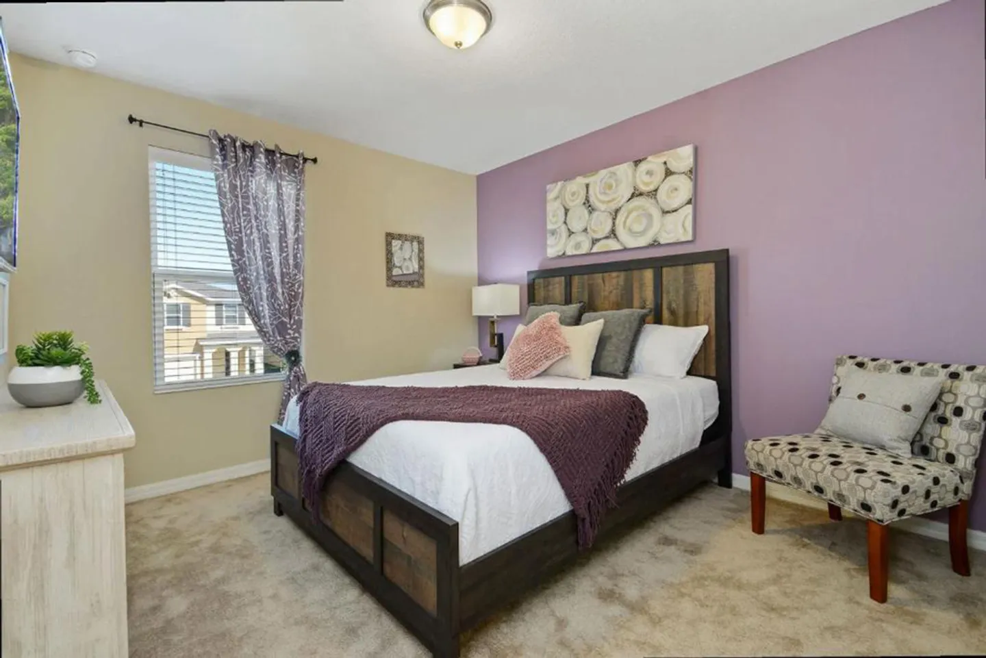 Bedroom featuring a wooden bed frame, a lavender accent wall, a patterned accent chair, and a window with blinds.