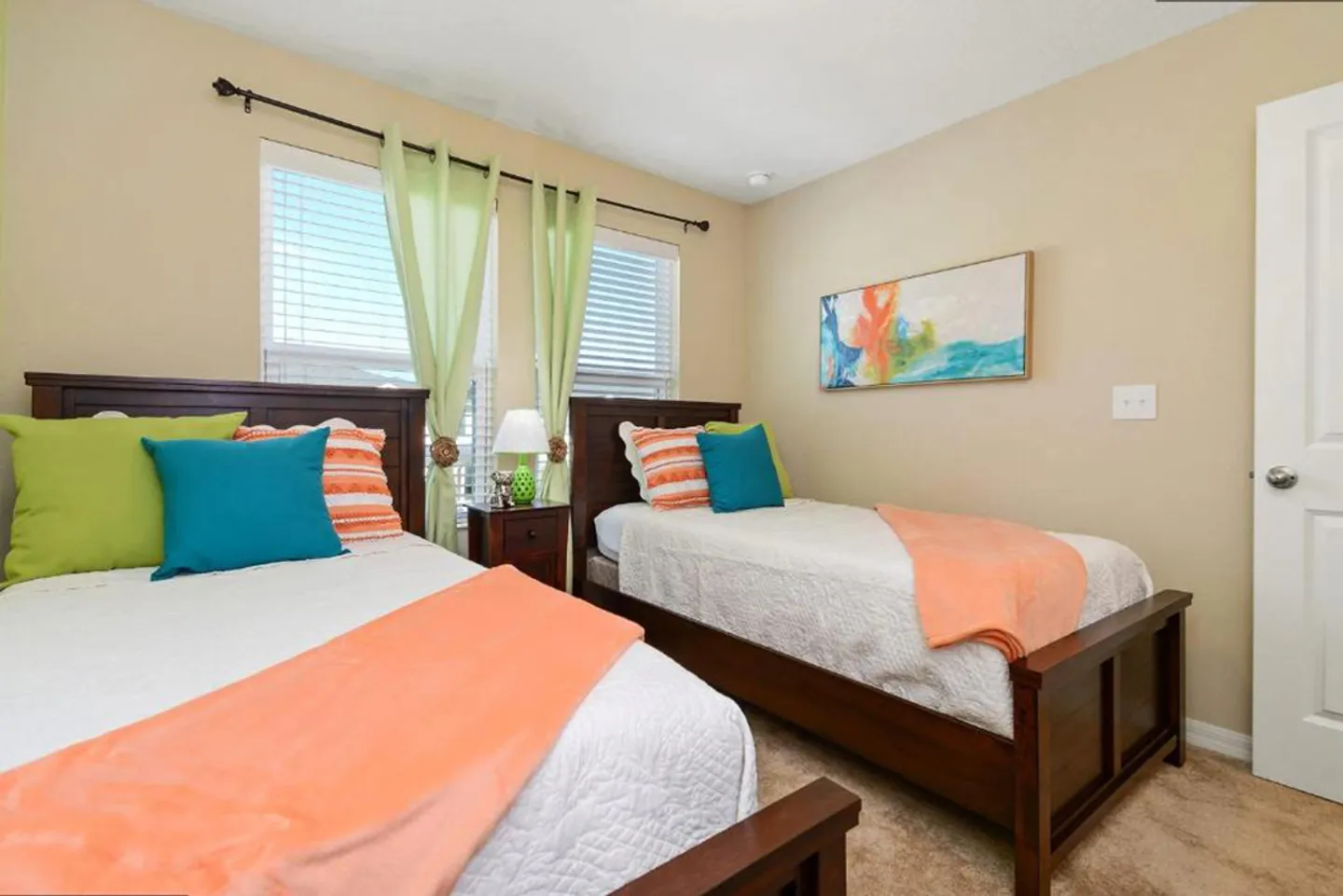 Bedroom with two twin beds dressed in white linens with colorful accent pillows and peach throws.