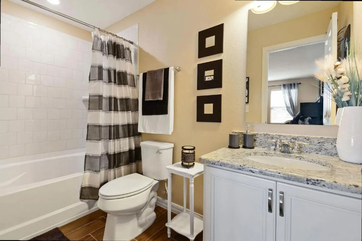Bathroom with a white vanity, speckled countertop, toilet, and bathtub with a striped shower curtain.