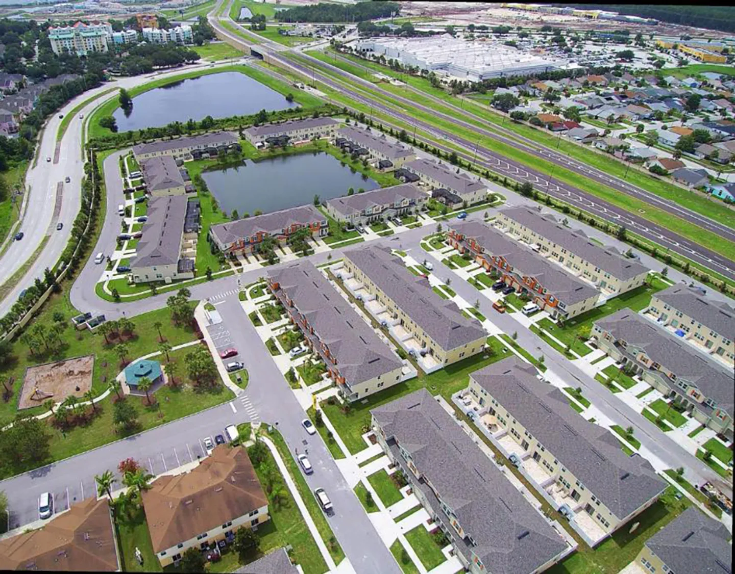 Aerial view of a residential townhouse community featuring retention ponds, paved roadways, and surrounding highways.