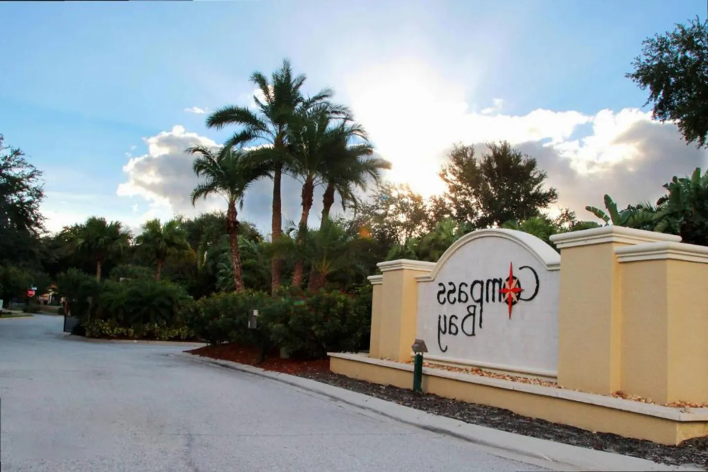 Community entrance sign for Compass Bay flanked by palm trees and landscaping along an asphalt drive.