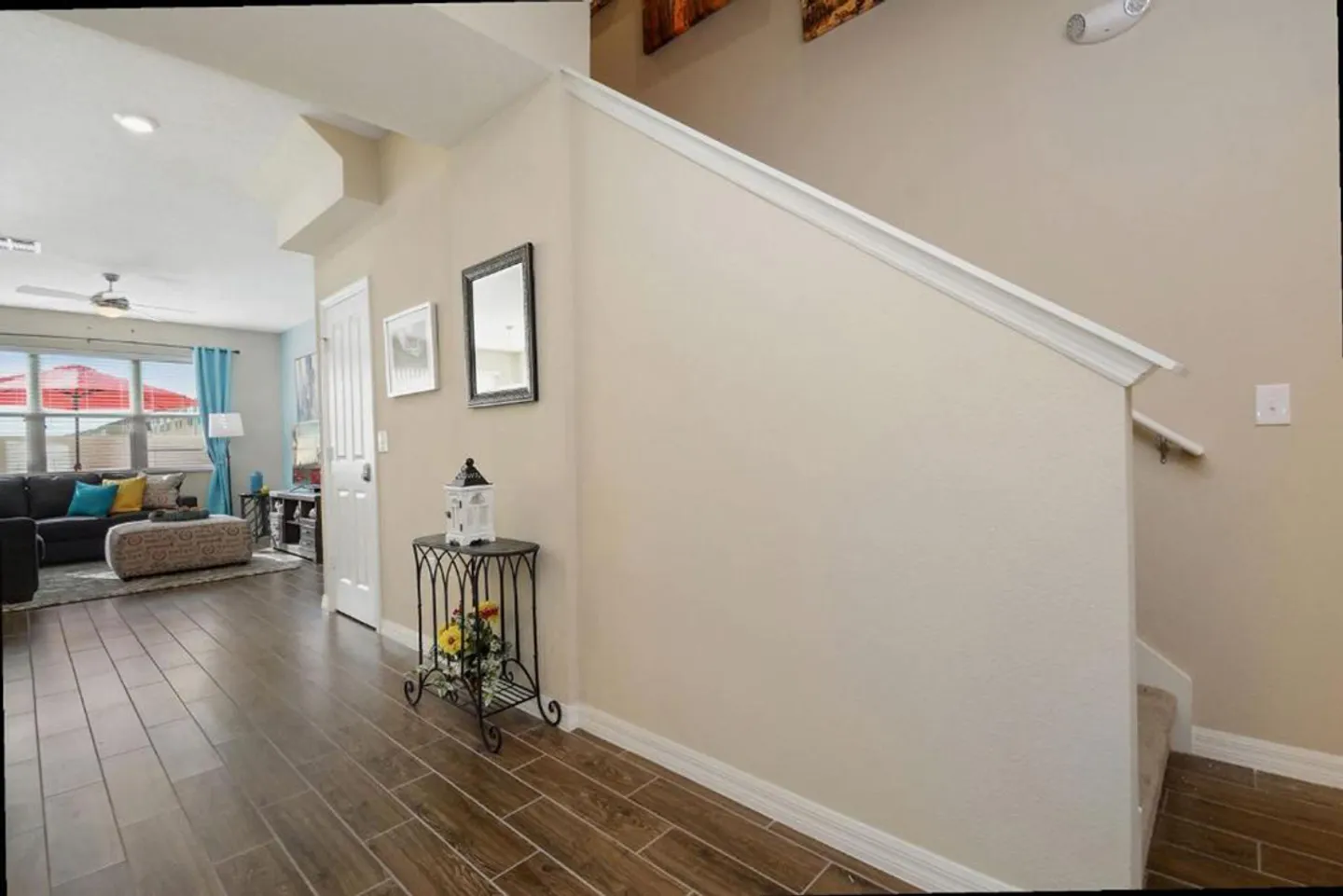 Hallway with wood-look tile flooring next to a staircase with a half wall, leading toward a furnished living room.