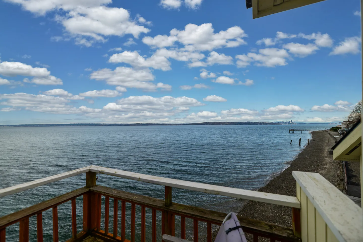 Elevated view from a wooden deck railing looking out over a shoreline and open water under a partly cloudy blue sky.