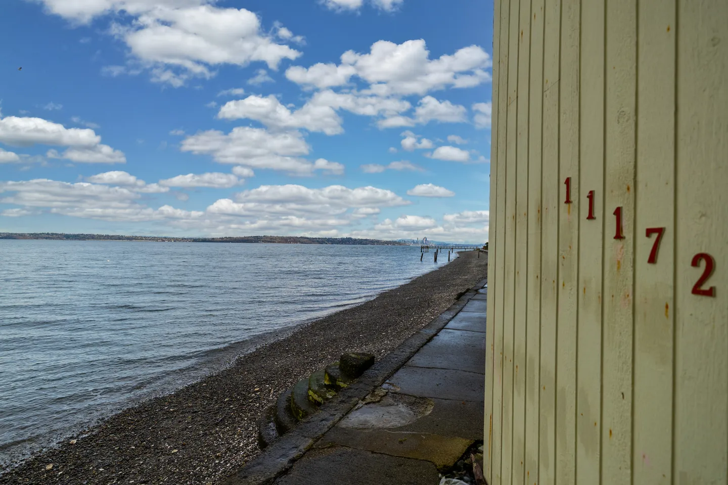 Exterior view along a waterfront path and pebble beach with house number 11172 on siding.