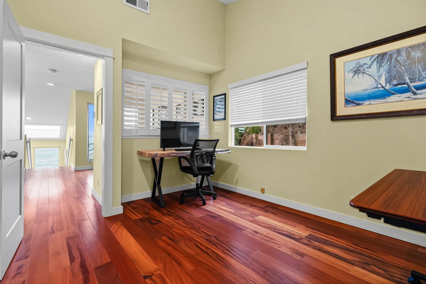 Dedicated workspace room with rich hardwood floors, live-edge wood desk, monitor, office chair, and shuttered windows.