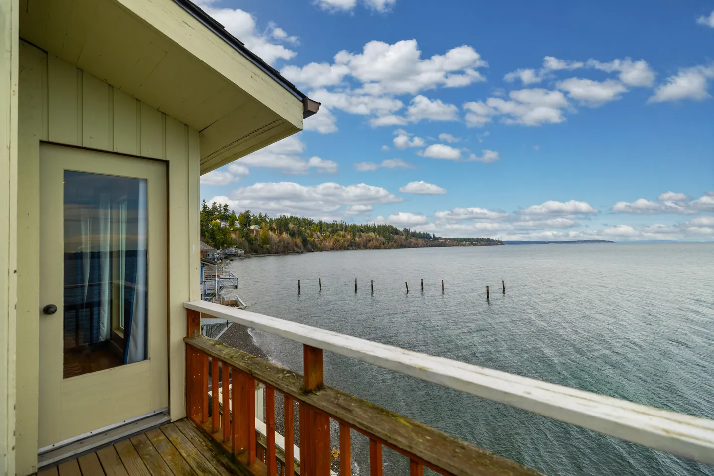 A wooden balcony with railings overlooks a wide expanse of ocean water under a partly cloudy blue sky.