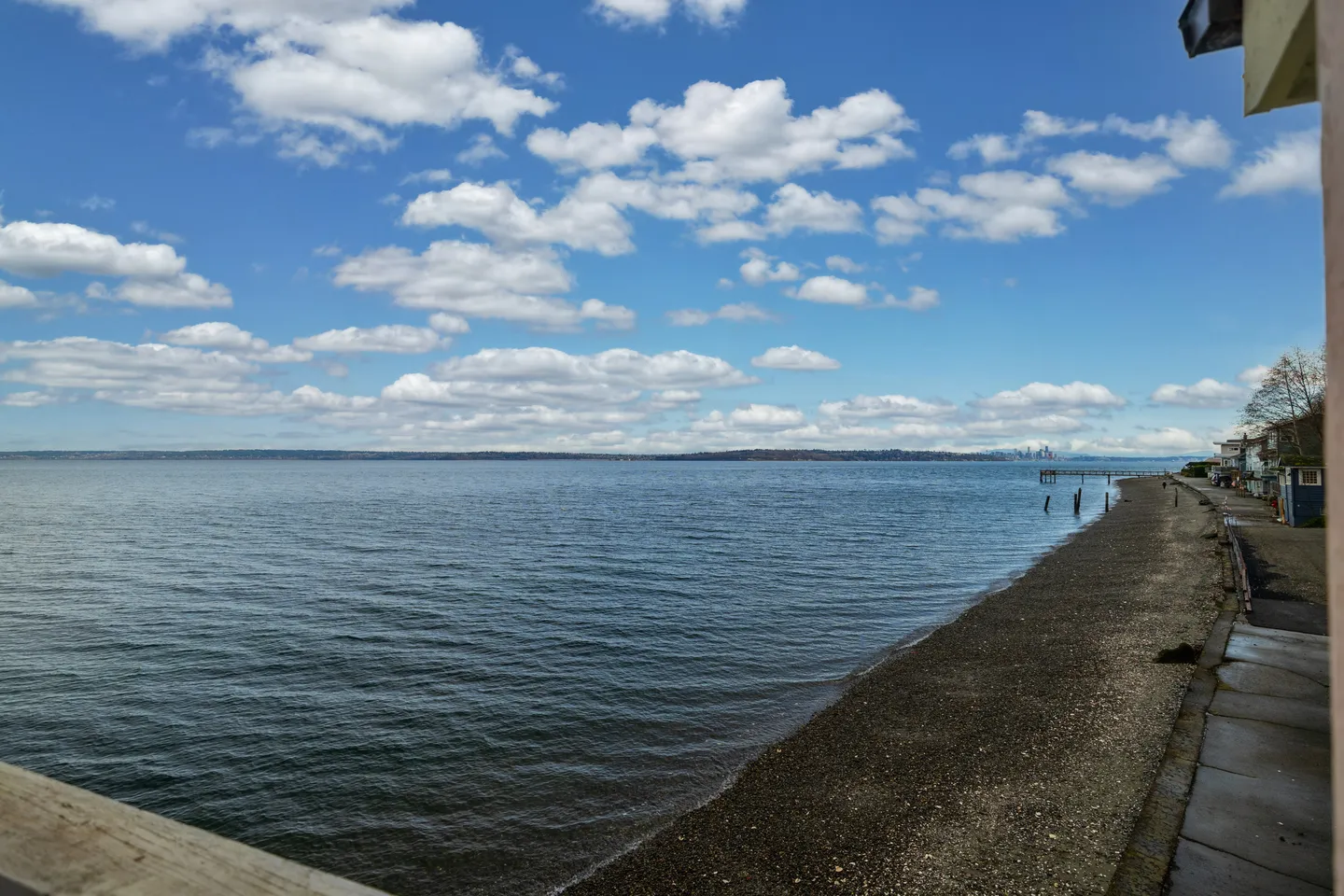 Elevated view overlooking a wide body of water and a pebbled shoreline under a blue sky with scattered clouds.
