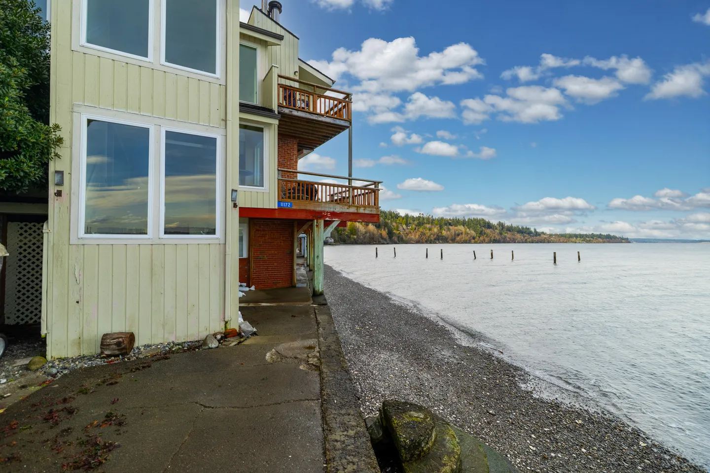 Exterior of a multi-story waterfront home with balconies directly adjacent to a pebbled beach and the water.