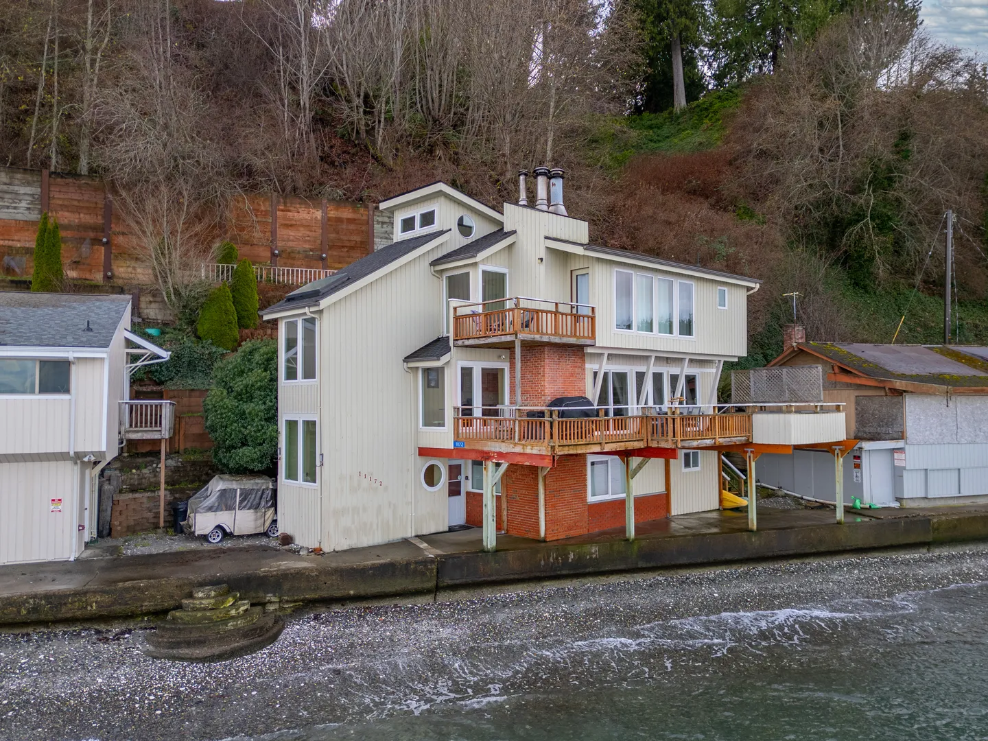 Exterior of a multi-story waterfront home with tiered wooden balconies situated right on the shore.