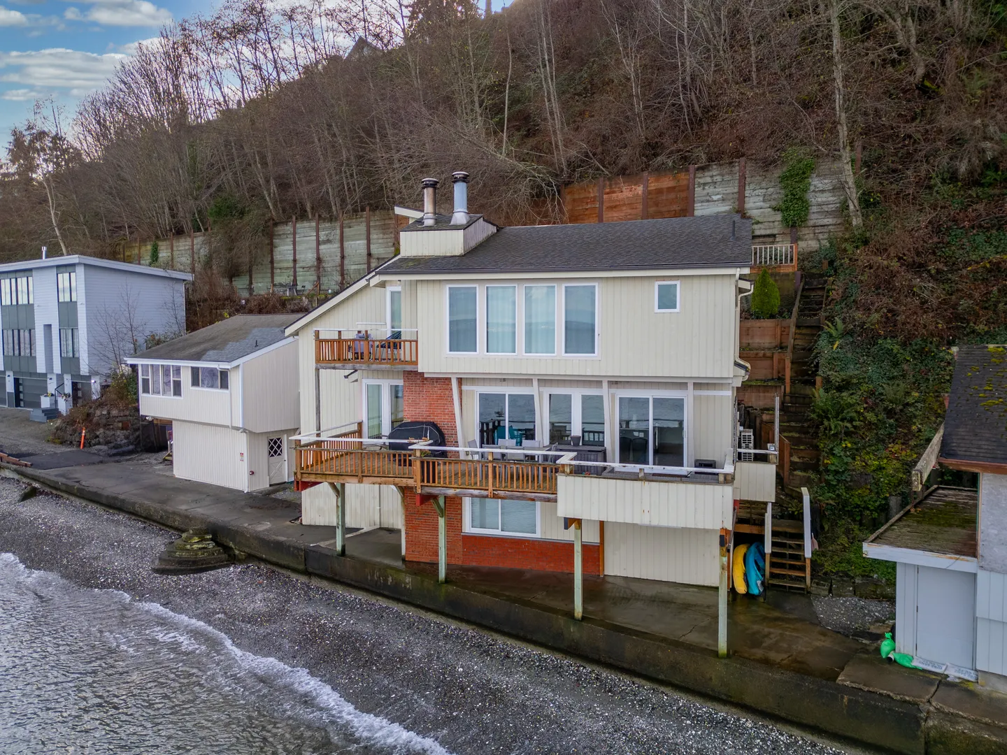 Exterior elevated view of a multi-story waterfront home with multiple decks right along a rocky shoreline and seawall.