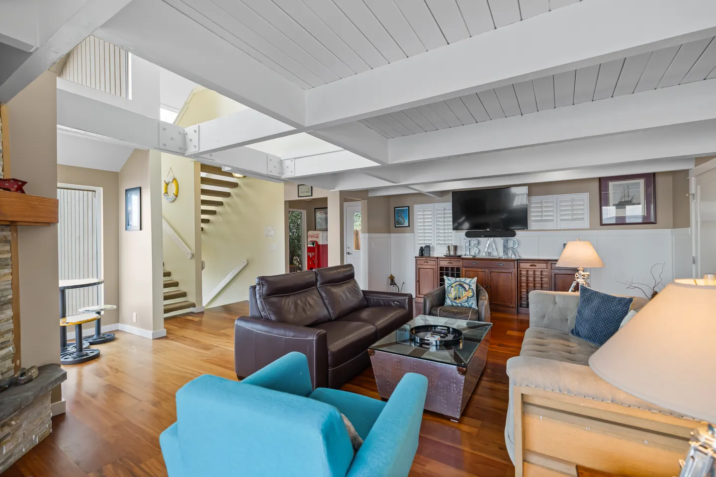 Living room with wood floors, white exposed ceiling beams, leather and fabric seating, and a mounted TV.