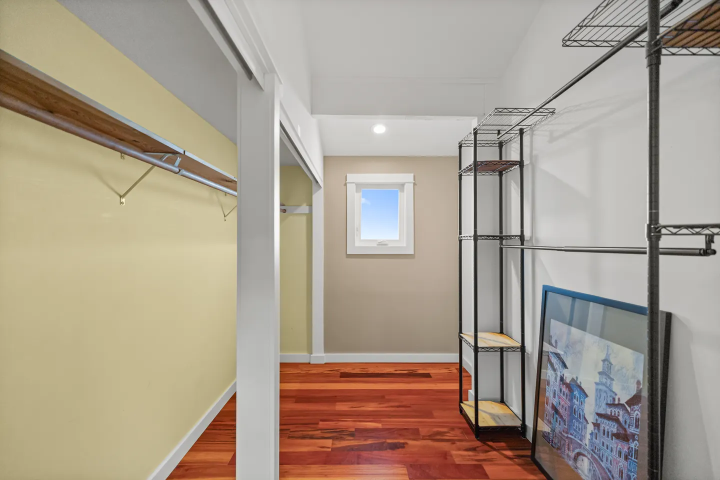 Walk-in closet area featuring hardwood floors, wire and wood shelving, and a small exterior window.