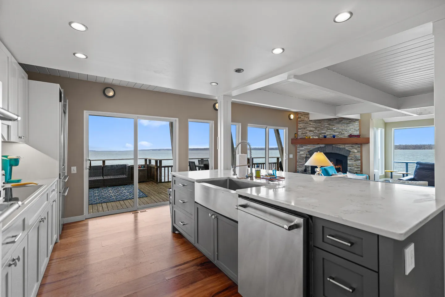 Open-concept kitchen with a large island and stainless steel apron sink, looking toward sliding glass doors to a deck overlooking the water.