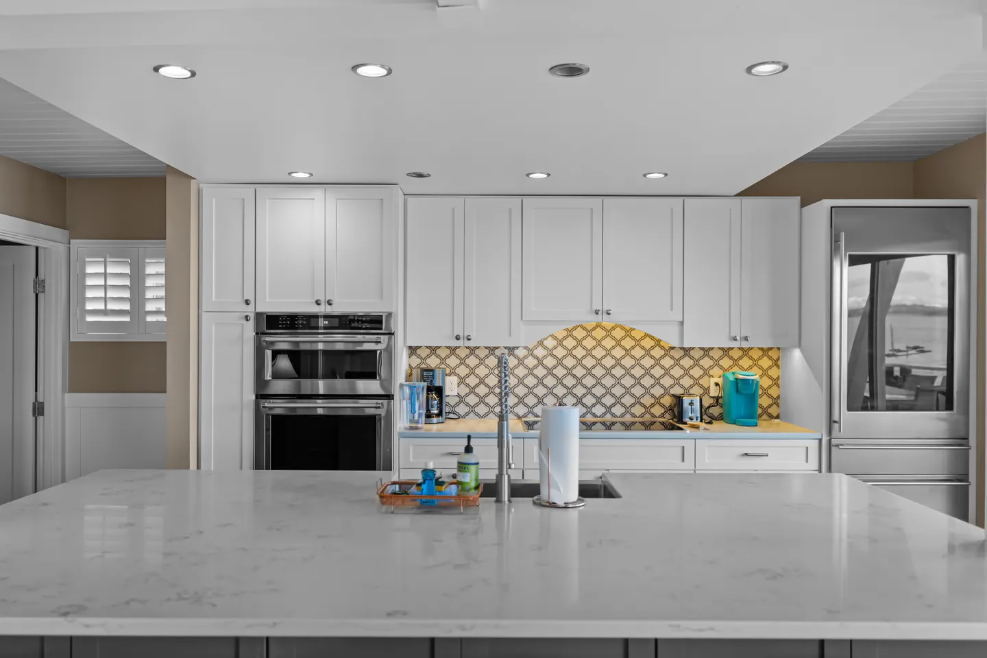 Kitchen featuring a large marbled island, white shaker cabinets, patterned tile backsplash, and stainless steel built-in appliances.