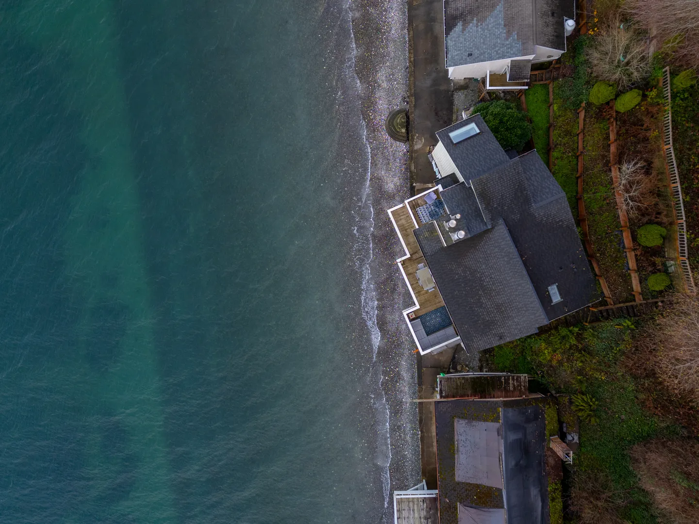 Overhead aerial view of a waterfront house directly on a rocky shoreline with dark blue water.