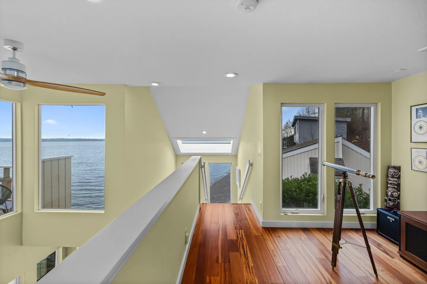 Upstairs landing with hardwood floors, a telescope on a tripod, and windows overlooking a body of water.