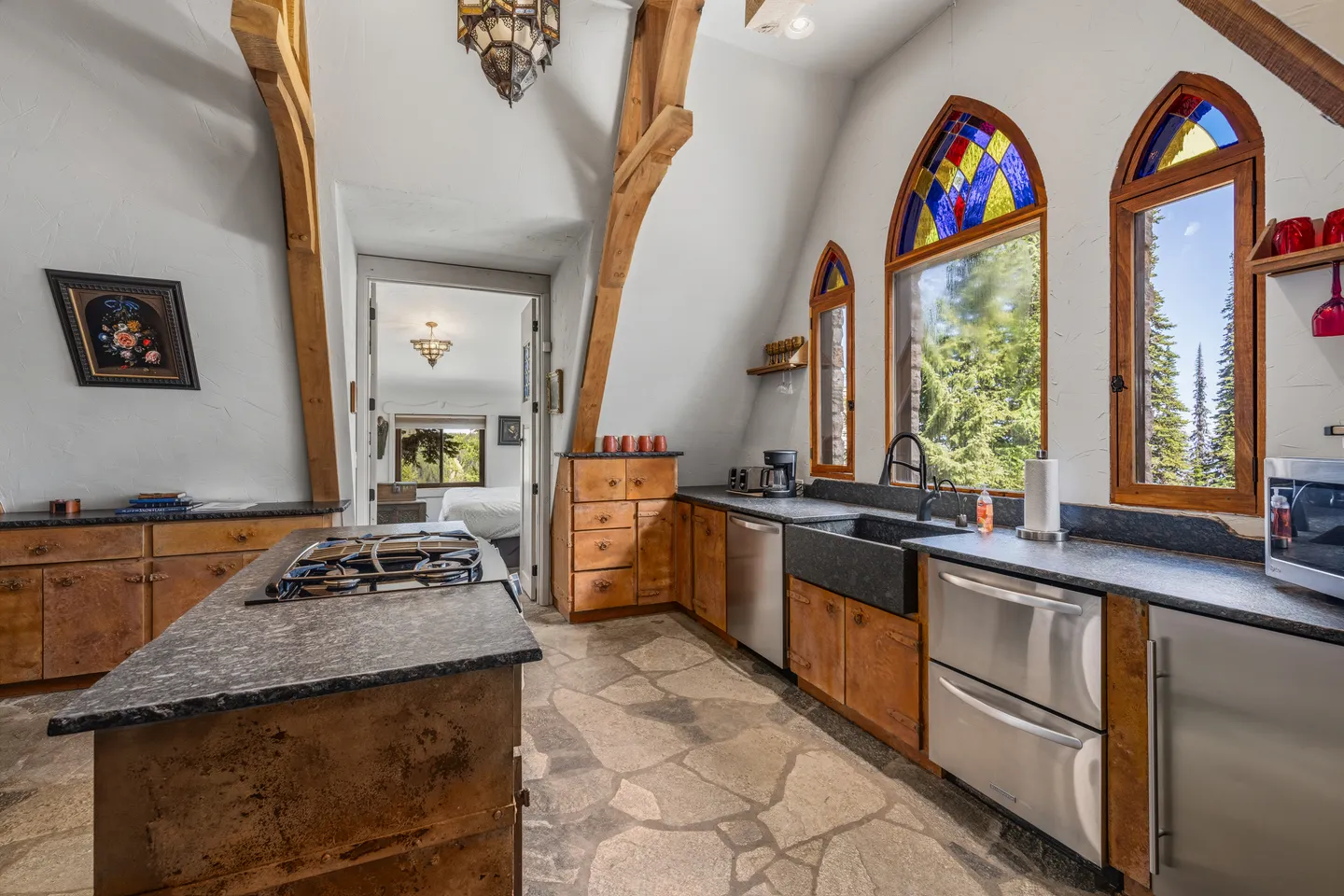 Kitchen with stone-look flooring, dark countertops, an island with a gas cooktop, and arched windows with stained-glass accents.