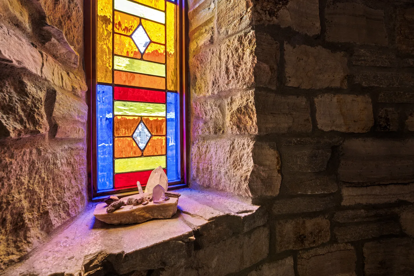 Stained-glass window set into a thick stone wall with crystals arranged on the deep stone sill.