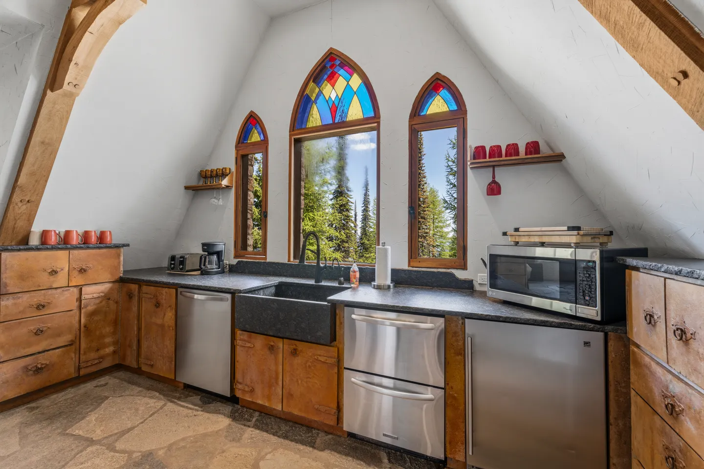 A kitchen nook with vaulted ceilings, wooden cabinets, stainless steel appliances, and arched windows featuring stained glass.