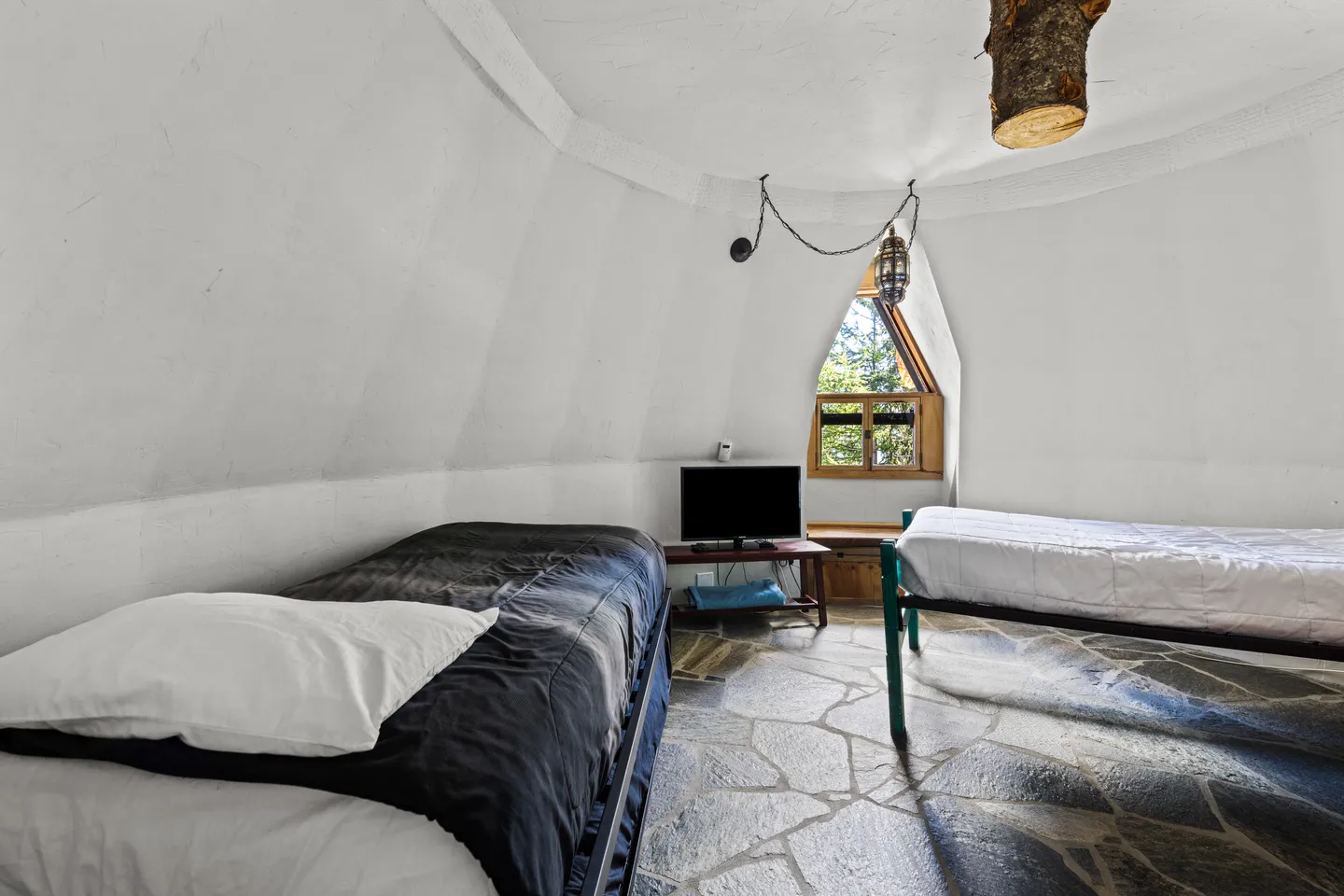 A bedroom inside a dome-shaped room with curved white walls, stone tile flooring, and two twin beds.